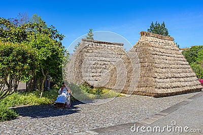 Rear part of two typical houses in the parish of Santana, covered with thatched roofs, a woman sitting knitting in the shade. Editorial Stock Photo