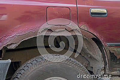Rear right wing and bottom of door with threshold of a serviceable maroon car covered with traces of metal corrosion and rust Stock Photo
