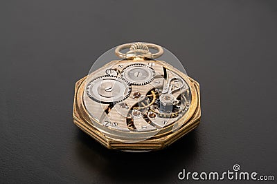 Rear viev of golden old pocket watch with open clockwork lying on a gray surface. Mechanism of golden vintage watch with Stock Photo