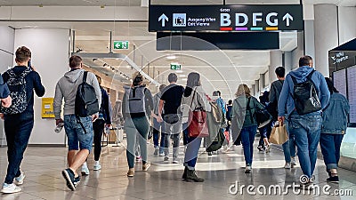 Rear view of air travellers walk through arrivals hall of Airport with backpacks and luggage Editorial Stock Photo