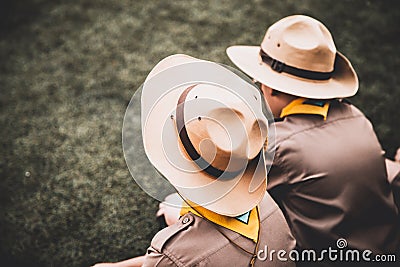 Rear view or backside of two Asian boy scout sitting on greensward for relax time. Editorial Stock Photo