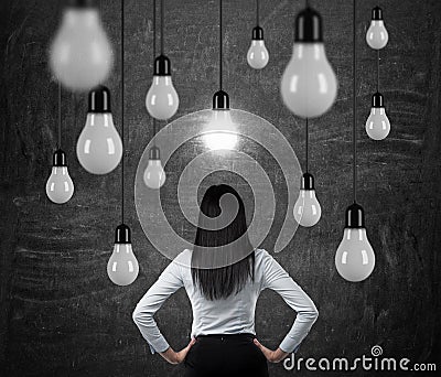 Rear view of the brunette lady who is looking at the hanging light bulbs. a concept of searching new ideas. Stock Photo