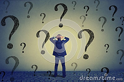 Rear view business man standing in front of wall with many questions Stock Photo