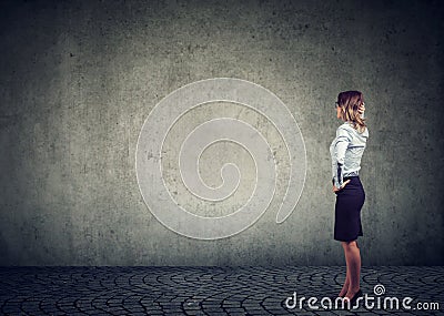 Rear view of business woman standing by the wall with hand on head wondering what to do next being challenged. Full length of Stock Photo