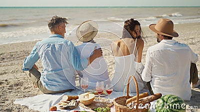 Rear view of couple friends at beach having picnic celebration with wine and tasty meal. Stock Photo