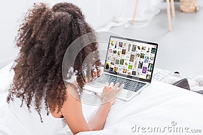 Rear view of curly woman using laptop with pinterest on screen in bed Editorial Stock Photo