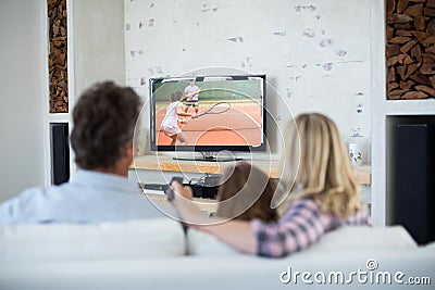 Rear view of family sitting at home together watching tennis match on tv Stock Photo