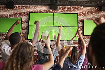 Rear View Of Friends Watching Game In Sports Bar On Screens Stock Photo