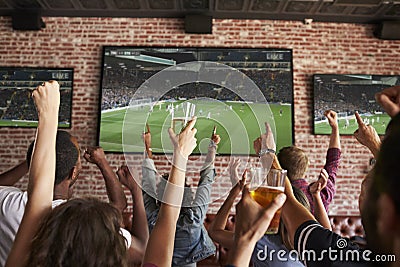 Rear View Of Friends Watching Game In Sports Bar On Screens Stock Photo