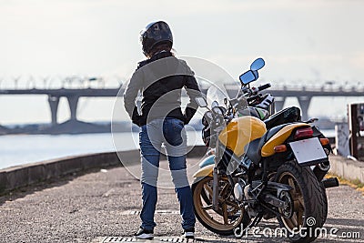 Rear view at girl biker in motorcycle helmet standing next to bikes on street sea embankment, full-length Stock Photo