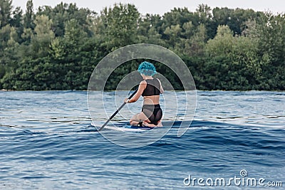 rear view of girl with blue hair sitting on paddle board Stock Photo