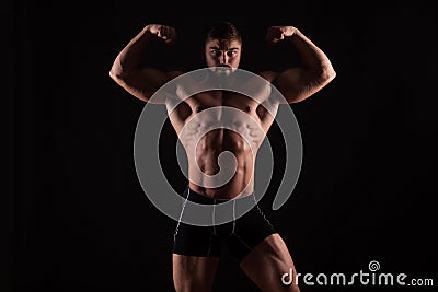 Rear view of healthy muscular young man with his arms stretched out isolated on black background Stock Photo