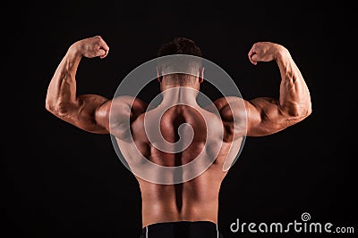 Rear view of healthy muscular young man with his arms stretched out isolated on black background Stock Photo