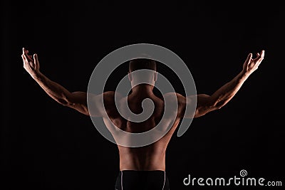 Rear view of healthy muscular young man with his arms stretched out isolated on black background Stock Photo