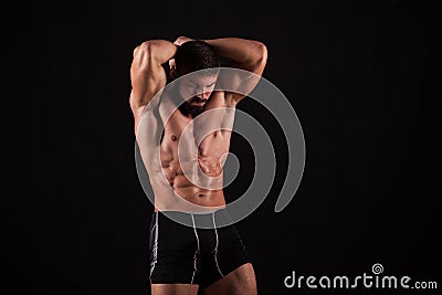 Rear view of healthy muscular young man with his arms stretched out isolated on black background Stock Photo