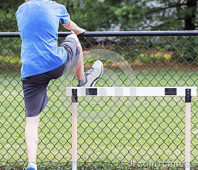 Hurdle runner performing a hurdle drill using a fence for support Stock Photo