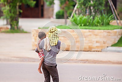 Rear view of Khmer mother holding son in her arms while across a street near construction site. Phnom Penh, Cambodia Editorial Stock Photo