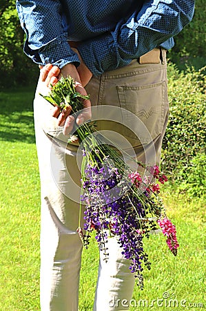 Rear view of a man, holding a bunch of flowers behind his back Stock Photo