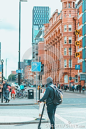 Rear view of a man riding a scooter on the street of Manchester City Centre, UK Editorial Stock Photo