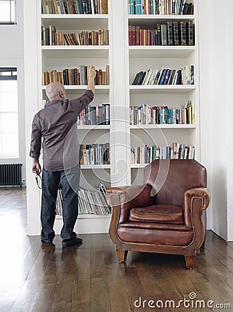Rear View Of Man Taking Book From Shelf Editorial Stock Photo