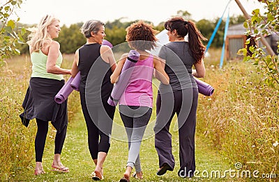 Rear View Of Mature Female Friends On Outdoor Yoga Retreat Walking Along Path Through Campsite Stock Photo