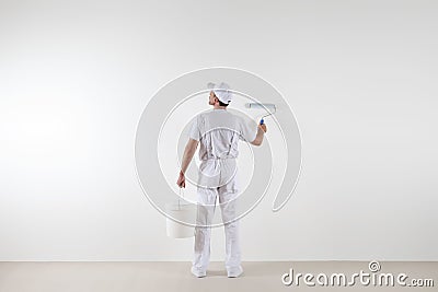 Rear view of painter man looking at blank wall, with paint roller and bucket, isolated on white room Stock Photo