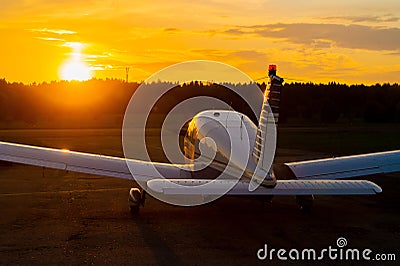 Rear view of a parked small plane on a sunset background. A silhouette of a grounded private jet at dusk. Piper Cherokee Stock Photo