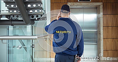 Rear view of security guard waiting for lift while standing in office building Stock Photo