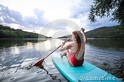 Rear view of senior woman paddleboarding on lake in summer. Stock Photo