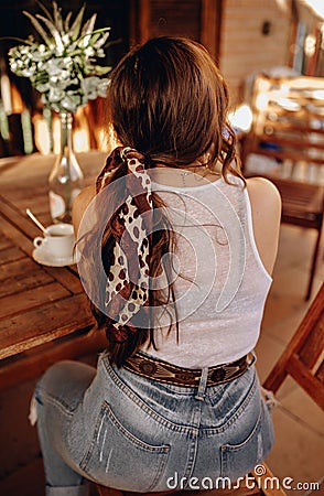 Rear view of a sexy young woman with a ponytail and a headband sitting on her back on a terrace drinking a cup of coffee in the Stock Photo