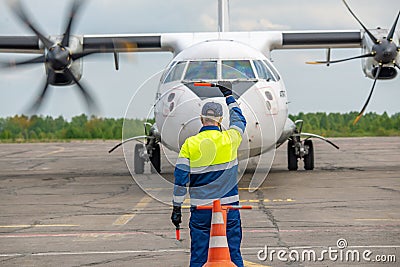 Rear view A signalman meets a passenger plane at the airport in front of propeller airplane. The plane is taxiing to the parking Stock Photo