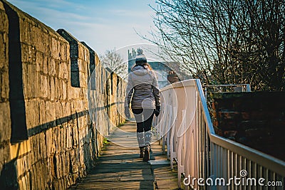 Rear view of a silhouette of a young woman walking along the city walls of York on a sunny day. Editorial Stock Photo