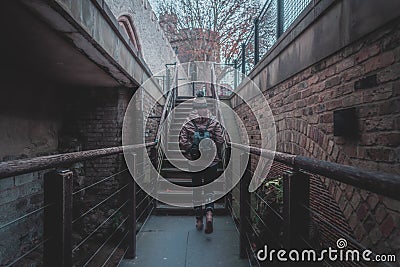 Rear view of silhouette of young woman walking through a stairway between old brick walls of an ancient castle on a cloudy and Editorial Stock Photo