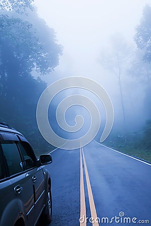 Rear view of silver SUV car on the asphalt road while through a misty mysterious tropical forest. Somewhere in North Thailand Stock Photo
