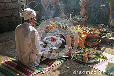 Rear view to Hindu priest praying during a wedding ceremony. Pedanda sits on the ground in front of the offerings and performs Editorial Stock Photo