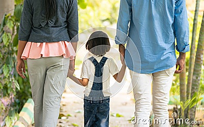 Rear view tracking shot of joyful excited jumping girl kid by holding parents hands at park - concept of family bonding Stock Photo