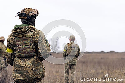 Rear view of two armed Ukrainian soldiers walking in steppe in uniform and helmets Stock Photo