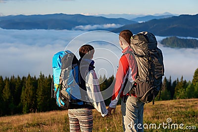 Rear view two persons holding hands enjoy the scenery of dense haze over mighty mountains Stock Photo