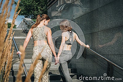 Rear view. Two young women in sportswear stand on city levels, steps, rest after training. Girls have break in exercises Stock Photo