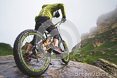 Rear view wide angle of a man on a mountain bike stands on a rocky terrain and looks at a rock. The concept of a Stock Photo