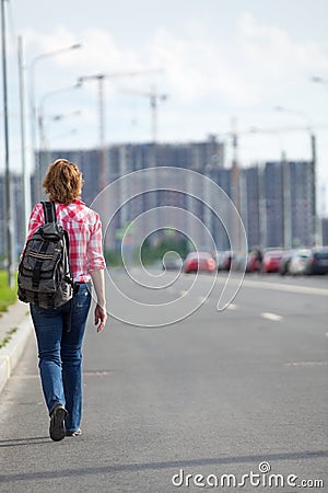 Rear view at woman hitchhiker walking on asphalt road in urban street, copyspace Stock Photo