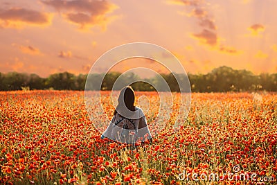 Rear view of woman walking in poppy meadow at sunset. Stock Photo