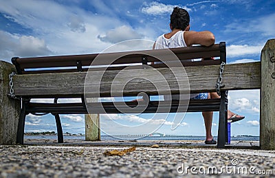 Rear view of a women sitting on a bench overlooking the great south bay in Babylon Village on a summer afternoon Stock Photo