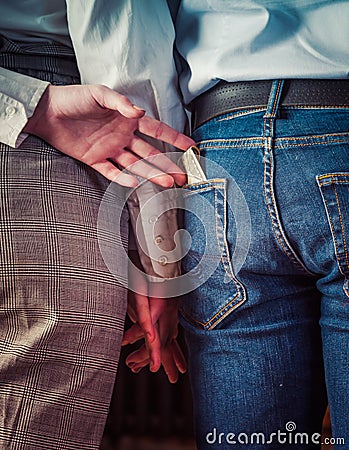 Rear View Of young couple holding hands, the second hand wife pulls money from the pocket of her husband`s denim trousers until h Stock Photo