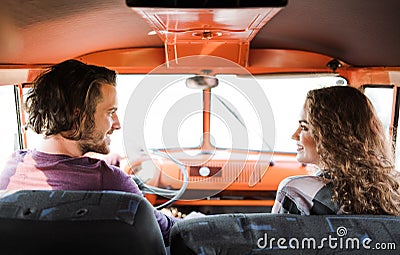 A rear view of young couple on a roadtrip through countryside, driving minivan. Stock Photo