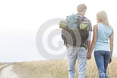 Rear view of young hiking couple holding hands while walking in countryside Stock Photo