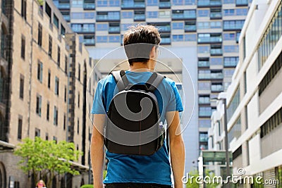 Rear view of a young man with backpack just arrived in a big city and looking to modern buildings with perspectives and Stock Photo