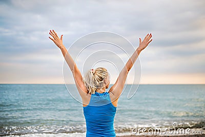 Rear view of young sporty woman runner in blue sportswear standing on the beach. Stock Photo