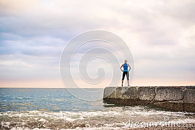 Rear view of young sporty woman standing on a pier by the ocean outside. Stock Photo