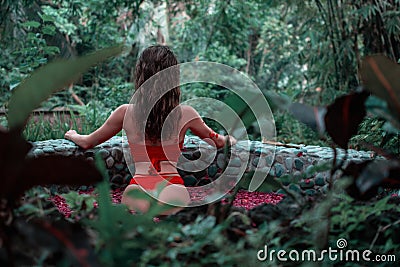 Attractive slim girl is standing back in the jungle. Brunette model in in the pool of flowers. Spa, relaxing. model Stock Photo